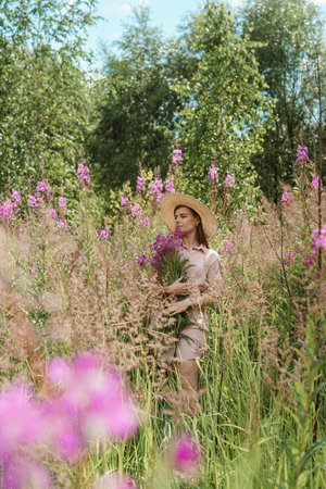 young woman in nature with a bouquet of pink wild flowers. A bouquet of Ivan-tea in the hands of a woman.の写真素材