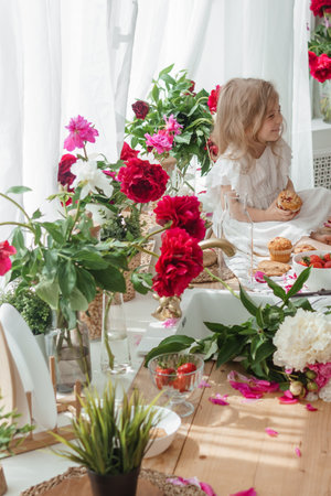 A little blonde girl on a kitchen countertop decorated with peonies. Spring atmosphere.の写真素材