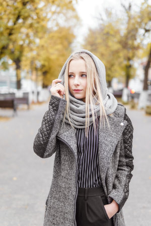 A young blonde walks through the autumn city in a gray coat. The concept of urban style and...