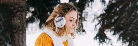 Teen blonde in a yellow sweater outside in winter. A teenage girl on a walk in winter clothes in a snowy forestの写真素材