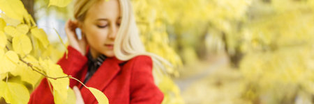 A young blonde woman walks around the autumn city in a red coat. The concept of urban style and lifestyle. Autumn portrait.の写真素材