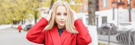 A young blonde woman walks around the autumn city in a red coat. The concept of urban style and lifestyleの写真素材