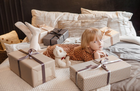 A little blonde girl is lying on a soft bed in a festive interior decorated in a New Years style. The child is waiting for a New Years gift.の写真素材