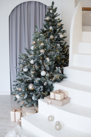 A large Christmas tree in the living room, decorated with garlands and light balloons. Bright Christmas interior with a white staircase.の写真素材