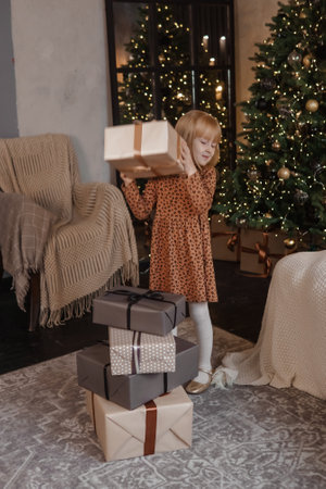 A little blonde girl in a festive interior decorated in a New Years style. A child holds a Christmas gift in a craft package.の写真素材