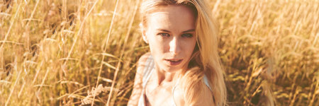 Beautiful blonde woman on a walk in a field with dry grass. A walk in nature, sunset in a field of pampas grass.の写真素材
