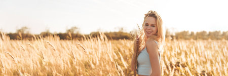 Beautiful blonde woman on a walk in a field with dry grass. A walk in nature, sunset in a field of pampas grass.の写真素材