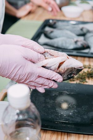 Raw Dorado fish on a black plate. Cooking Dorado in a cooking class. Raw fish, selective focus. Homemade food, cooking at home. Hands in the frame, the process of cooking fish.の写真素材