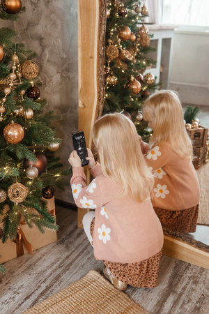 A little blonde girl photographs balloons on a Christmas tree in a festive interior decorated in a...