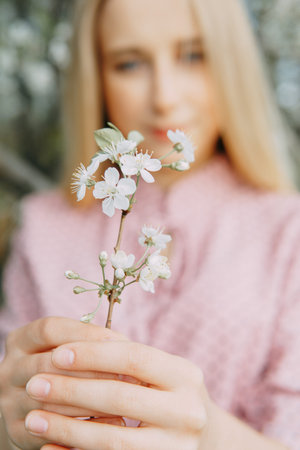 Blonde girl on a spring walk in the garden with cherry blossoms. Female portrait, close-up. A girl...