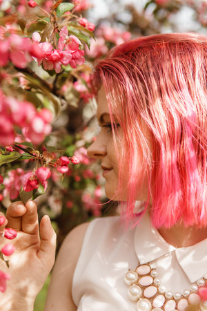Young girl with pink hair in an Apple orchard. Beautiful young girl in a blooming garden of pink Apple trees.の写真素材