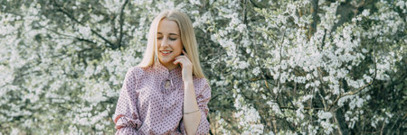 Blonde girl on a spring walk in the garden with cherry blossoms. Female portrait, close-up. A girl in a pink polka dot dressの写真素材