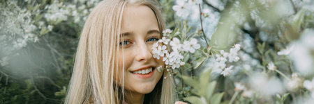Blonde girl on a spring walk in the garden with cherry blossoms. Female portrait, close-up. A girl in a pink polka dot dressの写真素材