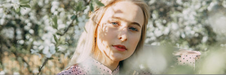 Blonde girl on a spring walk in the garden with cherry blossoms. Female portrait, close-up. A girl...