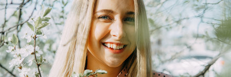 Blonde girl on a spring walk in the garden with cherry blossoms. Female portrait, close-up. A girl in a pink polka dot dressの写真素材