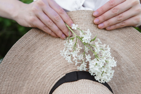 Womans Hands Holding a Straw Hat with White Flowers in a Natural Settingの写真素材