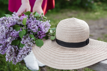 Close-up view of vibrant lilac flowers paired with a classic straw hat in a serene, green environment. The image conveys elegance, tranquility, and the beauty of nature during springtime.の写真素材