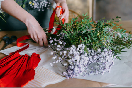 A florist works on preparing beautiful floral arrangement. Various flowers and materials lie on the table, emphasizing the artistic and inspiring atmosphere associated with floral design and presentation.の写真素材