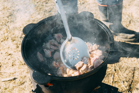 Meat cooking in a large cauldron outdoors over an open fire, a classic outdoor cooking concept for camping and traditional cuisineの写真素材