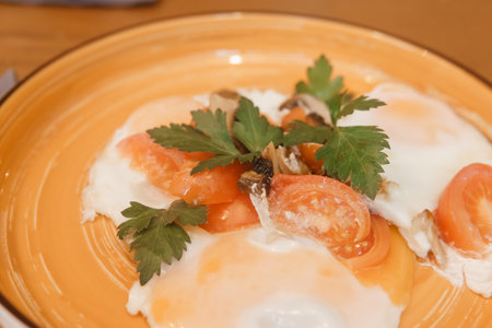 Freshly cooked delicious fried egg breakfast with chopped tomato, mushroom, and green parsley in orange bowl, top view. Healthy homemade mealの写真素材