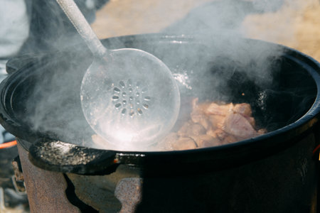 Meat cooking in a large cauldron outdoors over an open fire, a classic outdoor cooking concept for camping and traditional cuisineの写真素材