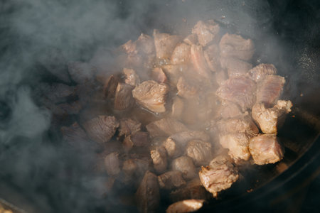 Pieces of meat frying in oil in a large cast iron cauldron with steam. Cooking outdoors in a big pot for holidayの写真素材