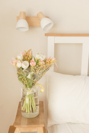Bouquet of tulips and mimosa flowers in a vase on a bedside table. Interior decoration with fresh flowers in a home settingの写真素材