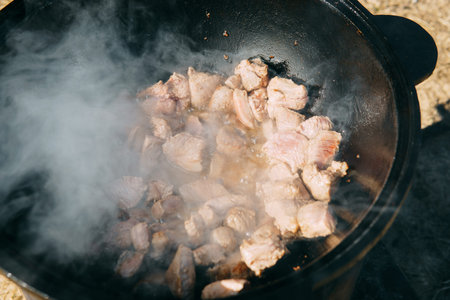 Pieces of meat frying in oil in a large cast iron cauldron with steam. Cooking outdoors in a big pot...