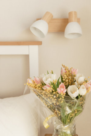 Bouquet of tulips and mimosa flowers in a vase on a bedside table. Interior decoration with fresh flowers in a home settingの写真素材