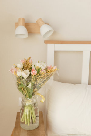 Bouquet of tulips and mimosa flowers in a vase on a bedside table. Interior decoration with fresh flowers in a home settingの写真素材
