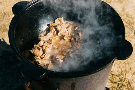 Pieces of meat frying in oil in a large cast iron cauldron with steam. Cooking outdoors in a big pot for holidayの写真素材