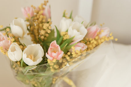 Elegant bouquet of white and pink tulips with yellow mimosa flowers in an interior setting. Fresh spring bloom for holiday celebrationの写真素材