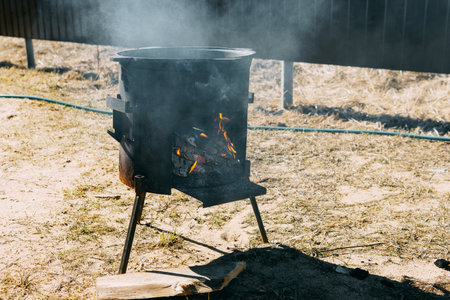 Steel kazan, a large cast iron cauldron, on a fire pit for cooking outdoors. Outdoor cooking concept with wood burning stoveの写真素材