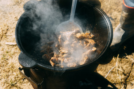 Meat cooking in a large cauldron outdoors over an open fire, a classic outdoor cooking concept for camping and traditional cuisineの写真素材