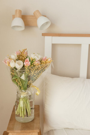 Bouquet of tulips and mimosa flowers in a vase on a bedside table. Interior decoration with fresh...