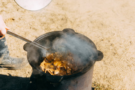 Meat cooking in a large cauldron outdoors over an open fire, a classic outdoor cooking concept for camping and traditional cuisine.の写真素材