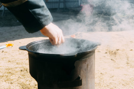 Person cooking in a cauldron with steam rising. Outdoor food preparation in a cast iron pot on a sunny day. Rustic meal concept.の写真素材