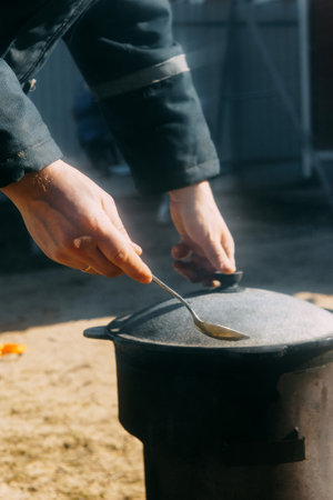 Person cooking in a cauldron with steam rising. Outdoor food preparation in a cast iron pot on a sunny day. Rustic meal concept.の写真素材