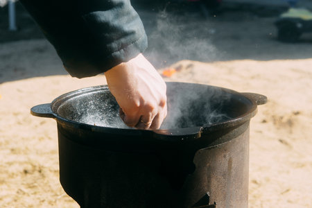 Person cooking in a cauldron with steam rising. Outdoor food preparation in a cast iron pot on a sunny day. Rustic meal conceptの写真素材
