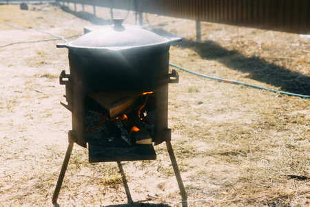 Steel kazan, a large cast iron cauldron, on a fire pit for cooking outdoors. Outdoor cooking concept with wood burning stoveの写真素材