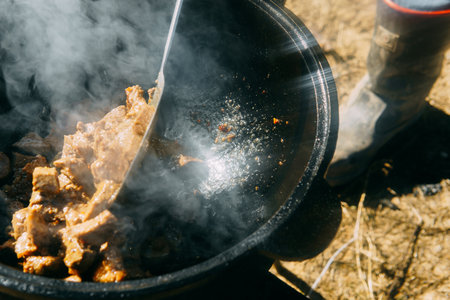 Pieces of meat frying in oil in a large cast iron cauldron with steam. Cooking outdoor in a big pot for holiday.の写真素材