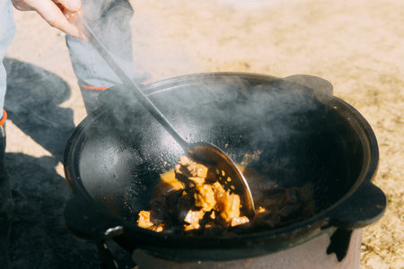 Meat cooking in a large cauldron outdoors over an open fire, a classic outdoor cooking concept for...
