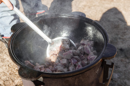 Meat cooking in a large cauldron outdoors over an open fire, a classic outdoor cooking concept for...