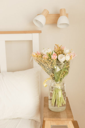 Bouquet of tulips and mimosa flowers in a vase on a bedside table. Interior decoration with fresh...