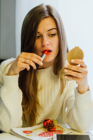 Woman applying red lipstick while looking in a compact mirror. Makeup application concept for beauty and cosmetic advertising.の写真素材