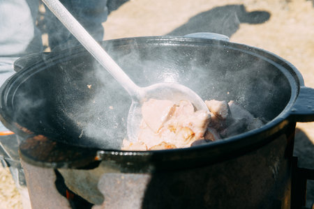 Meat cooking in a large cauldron outdoors over an open fire, a classic outdoor cooking concept for...