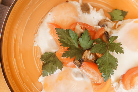 Freshly cooked delicious fried egg breakfast with chopped tomato, mushroom, and green parsley in orange bowl, top view. Healthy homemade meal.の写真素材