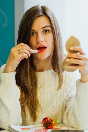 Woman applying red lipstick while looking in a compact mirror, beauty routine and cosmetic product concept.の写真素材