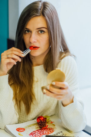 Woman applying red lipstick while looking in a compact mirror, beauty routine and cosmetic product concept.の写真素材