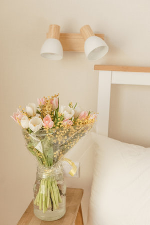 Bouquet of tulips and mimosa flowers in a vase on a bedside table. Interior decoration with fresh flowers in a home settingの写真素材